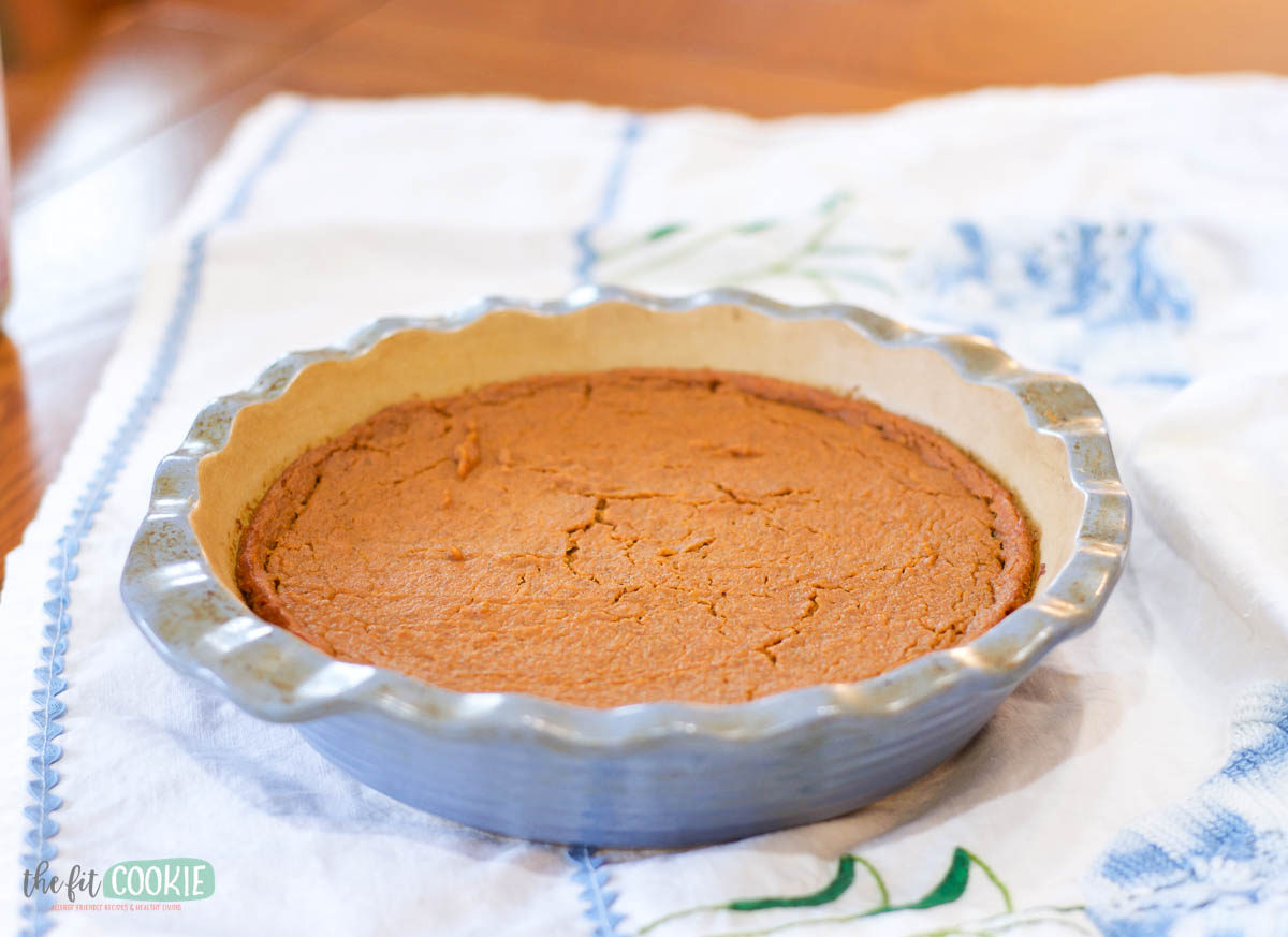 A crustless pumpkin pie is baked in a fluted ceramic dish and sits on a white and blue patterned cloth.
