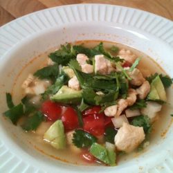 A bowl of soup with chicken, tomatoes and avocado.