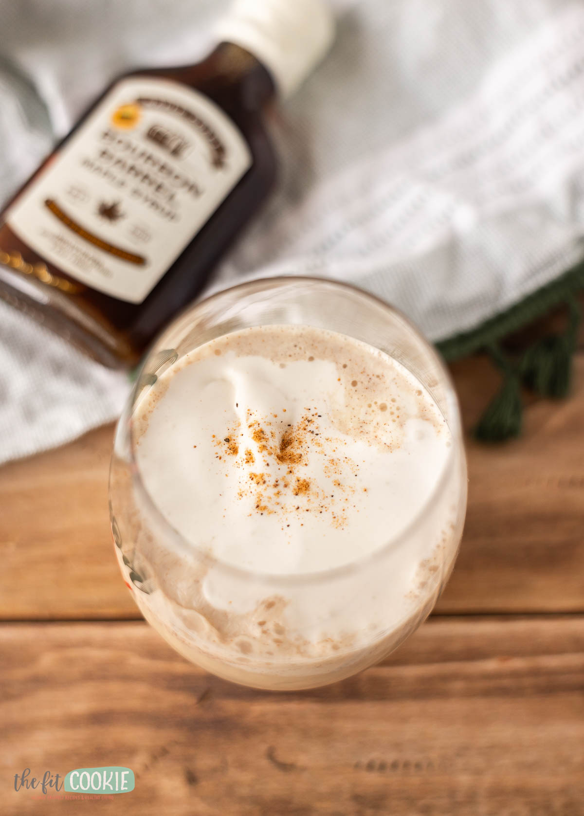A glass of vegan eggnog on a table with whipped cream and a sprinkle of nutmeg on top.