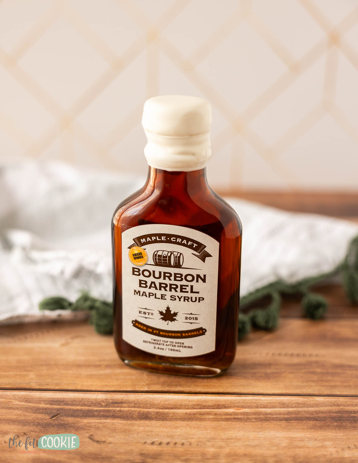 A mini bottle of Maple Craft Bourbon Barrel Maple Syrup sits on a wooden surface.