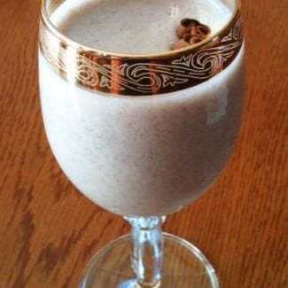 A glass filled with dairy-free egg nog on top of a wooden table.