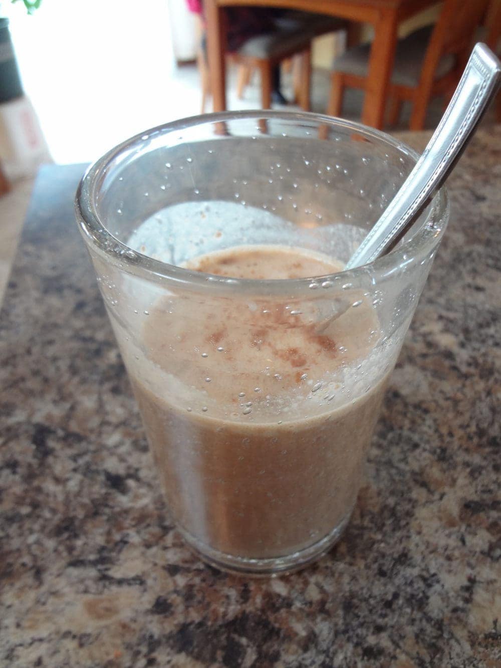 A mocha protein shake served in a glass cup with a spoon.