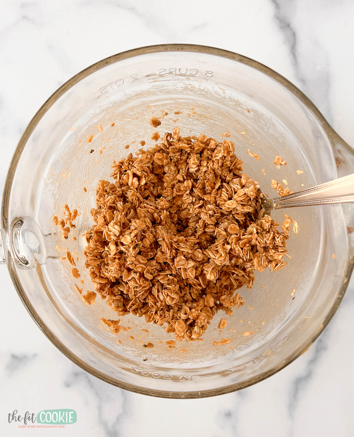A glass mixing bowl containing a mixture of oats and maple sunbutter mixture.