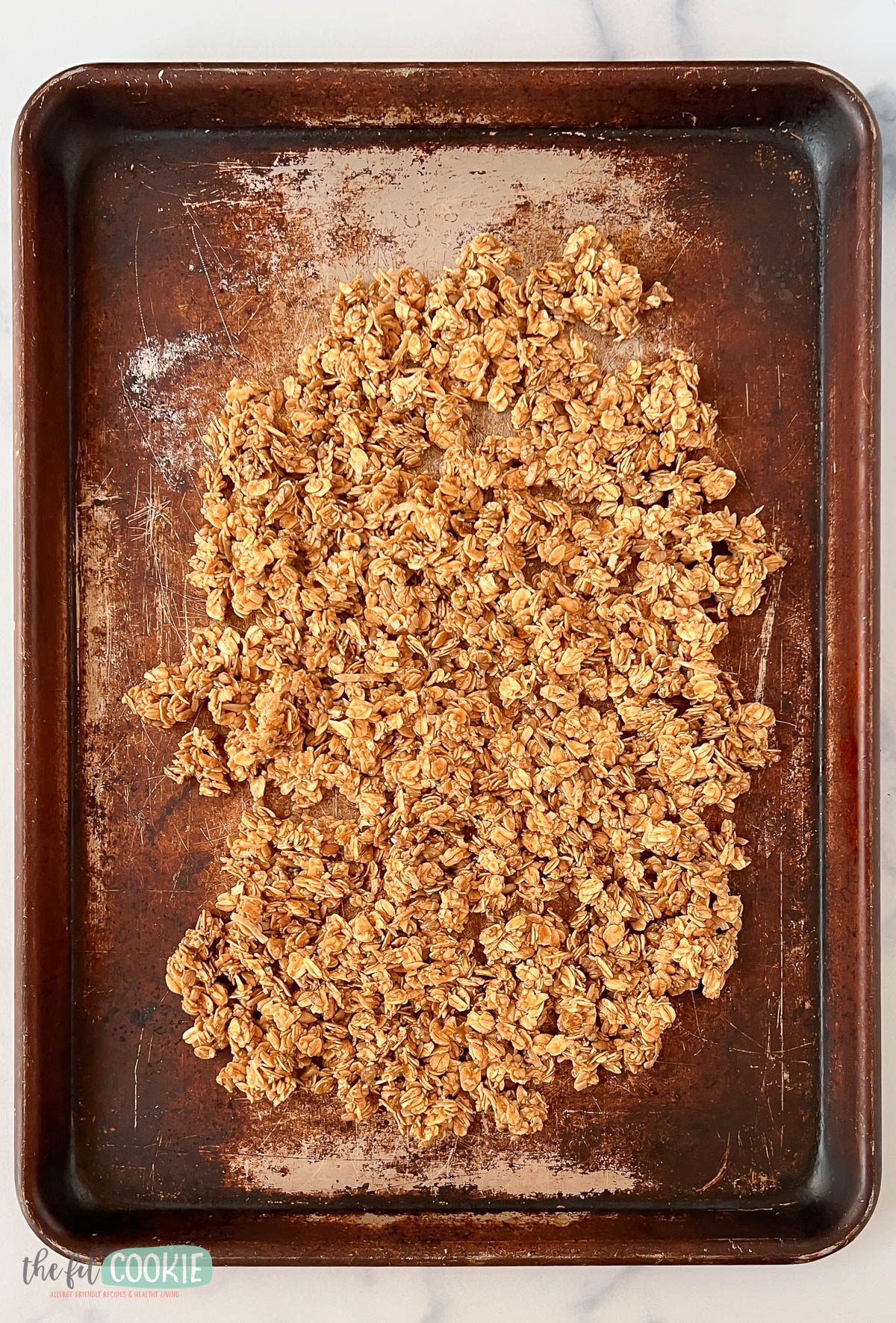 A baking sheet with a layer of maple sunbutter granola spread out on it, ready to be baked.
