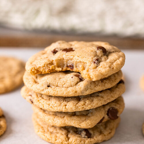 A tempting stack of five chocolate chip cookies rests on parchment paper, with a tantalizing bite taken out of the top cookie.