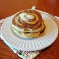 A stack of three cinnamon roll pancakes topped with melting butter on a white plate.