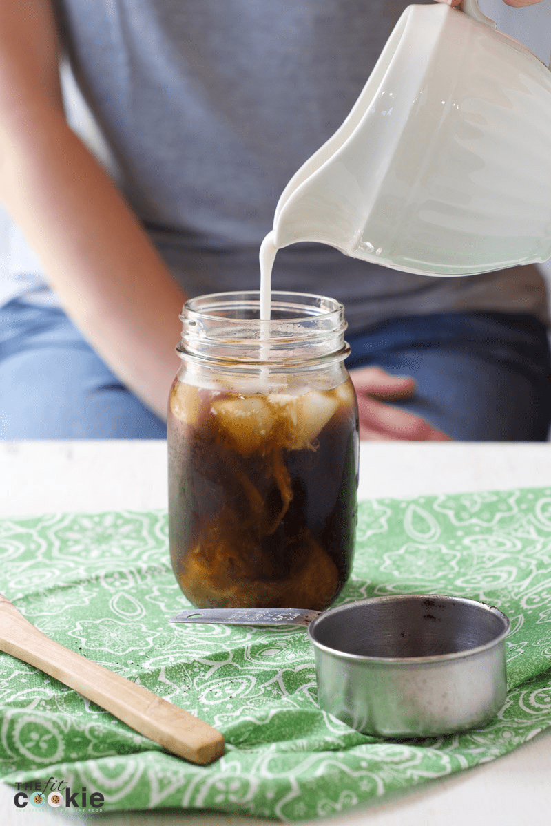 pouring coconutmilk from a white creamer dish into a cup of cold brew coffee