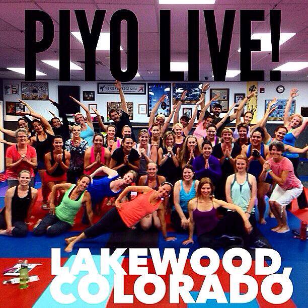 A large group of people pose together on exercise mats under the banner "PIYO LIVE!" proudly showcasing their PiYo spirit, with "LAKEWOOD, COLORADO" in bold text at the bottom.