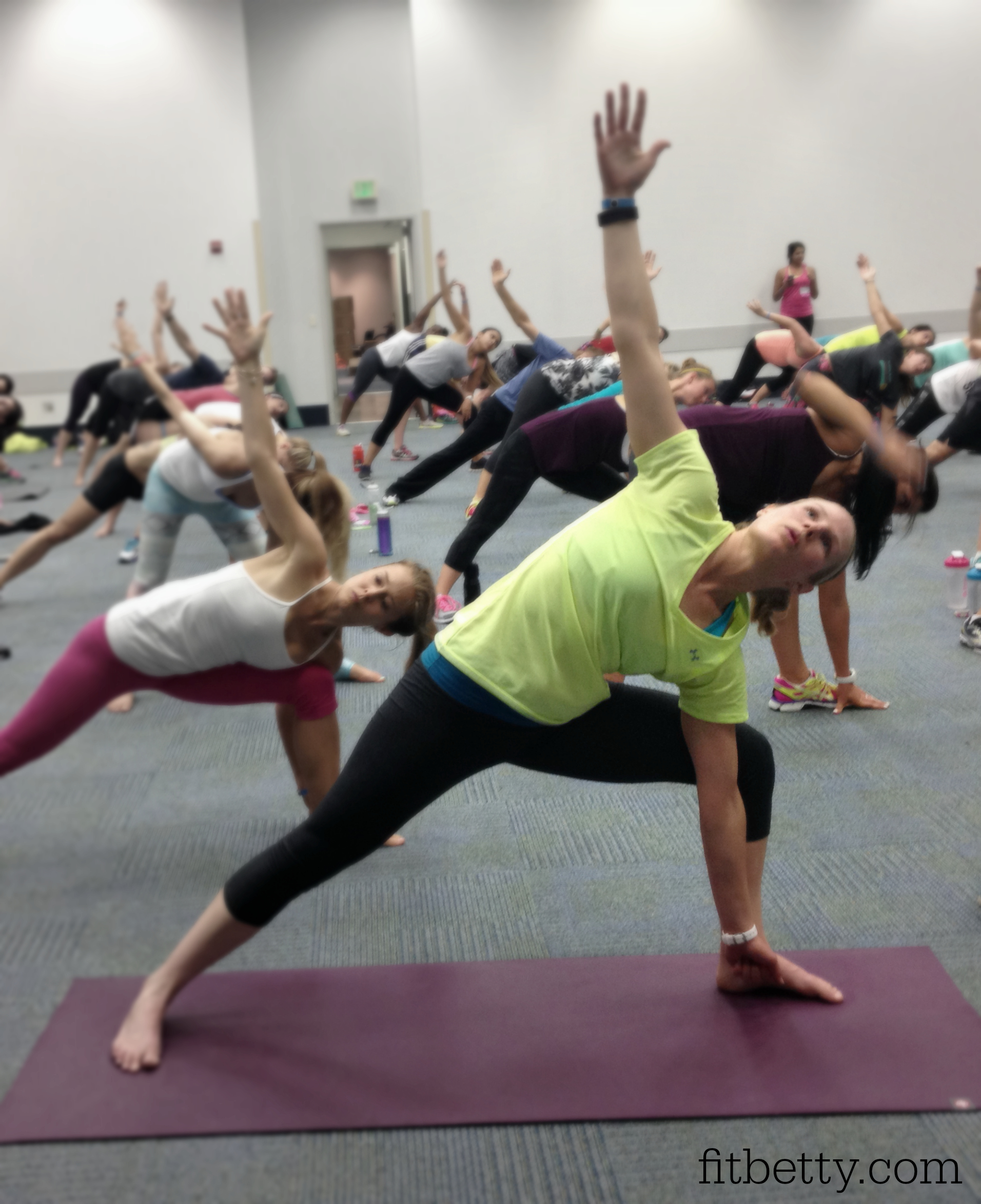 A group of people practice PiYo indoors, performing a side angle pose on mats in a spacious room.
