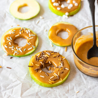 Donuts covered in caramel and sprinkles on a baking sheet.