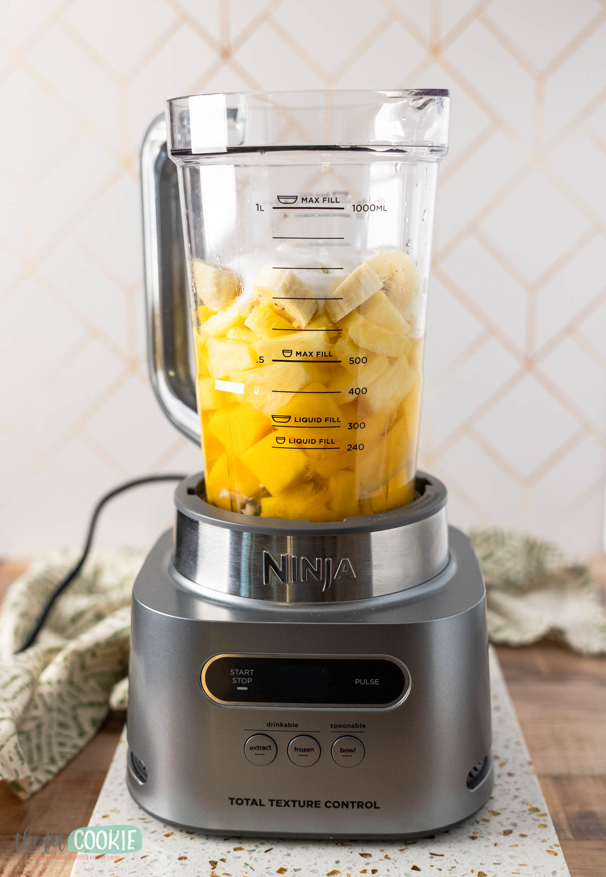 A Ninja blender filled with chopped pineapple and banana sits on a countertop, ready to blend into a delicious tropical smoothie.