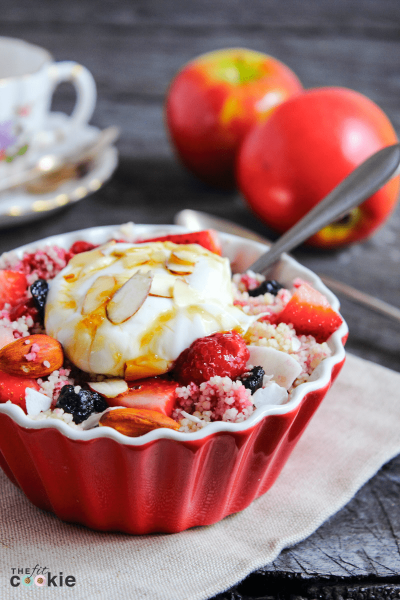 red bowl filled with dairy free mixed berry breakfast couscous topped with dairy free yogurt.