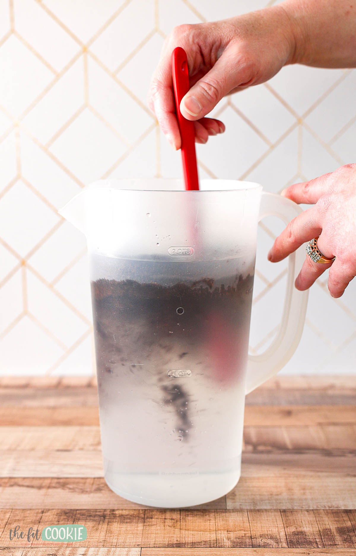 A person stirs coffee grounds into a pitcher of water.