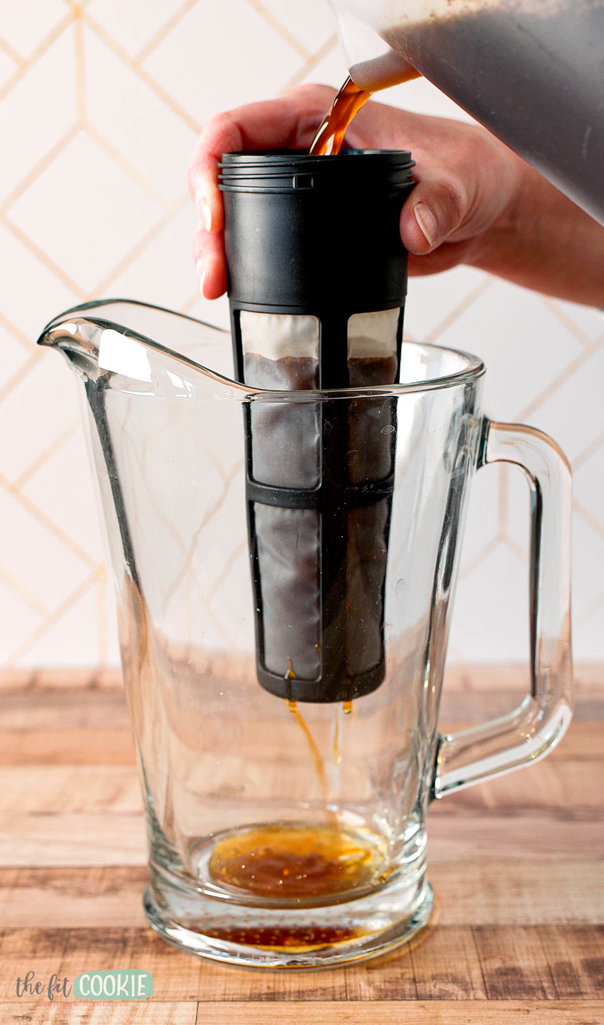 a person pours coffee through a mesh strainer into a pitcher.