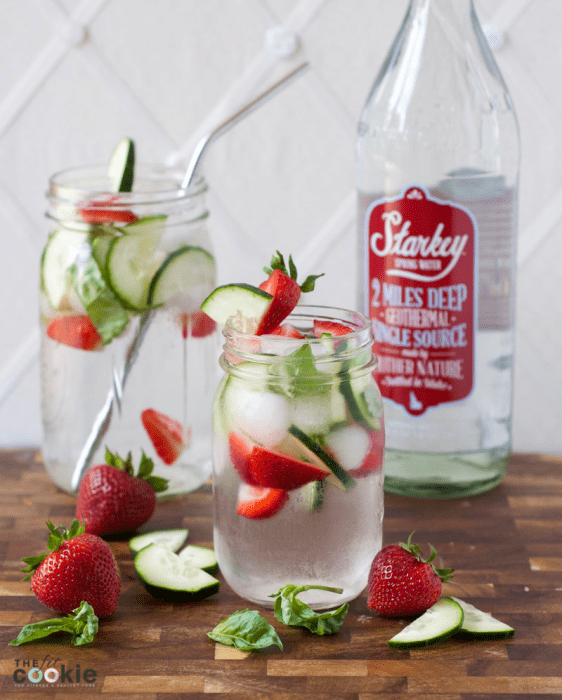 jars of fruit infused water surrounded by strawberry, basil, and cucumber