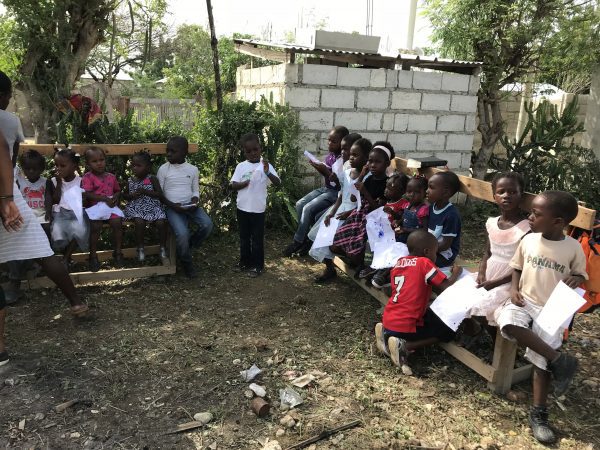 2 benches of Haitian students outside school ready to do a coloring project 