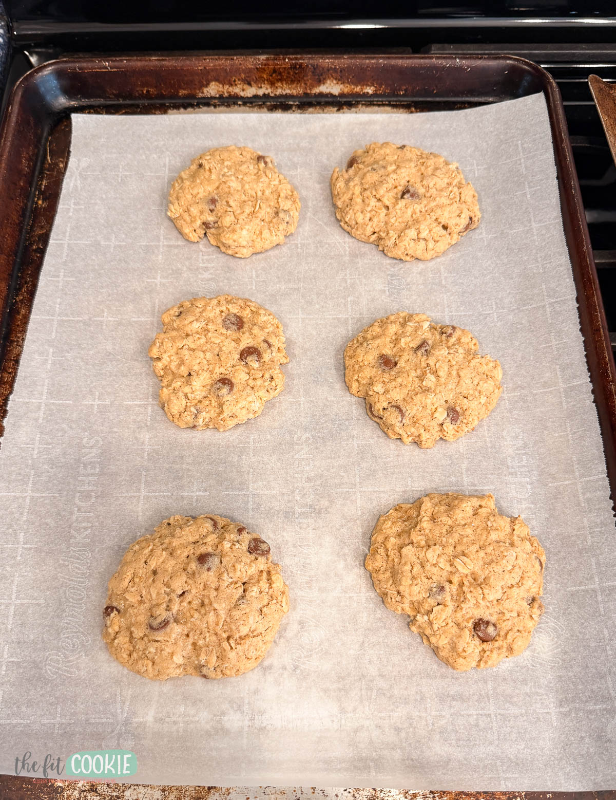 gluten free oatmeal cookies that are slightly misshapen on a baking sheet. 
