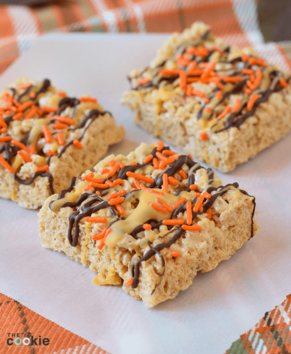 close up photo of dairy free gluten free pumpkin spice rice crispy treats on parchment paper with chocolate drizzle and sprinkles