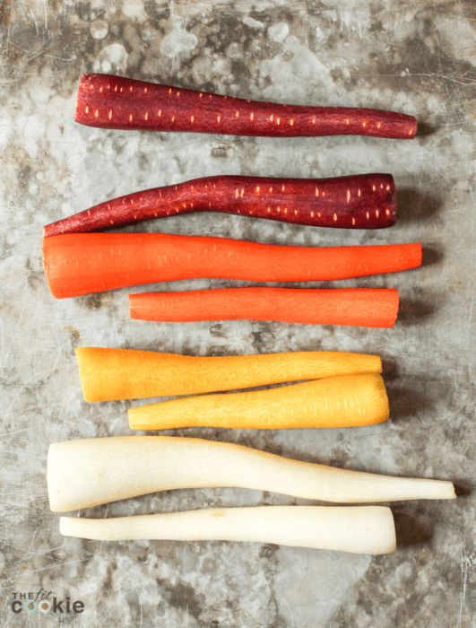 peeled uncooked rainbow carrots on a baking sheet