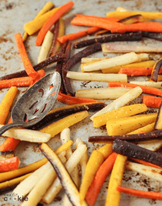 garlic roasted rainbow carrots on a baking sheet with a serving spoon