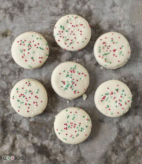 overhead photo of dairy free white chocolate ritz cookies on a baking sheet topped with christmas sprinkles