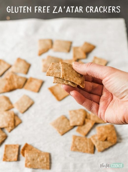 hand holding some gluten free za'atar crackers in front of a piece of parchment paper