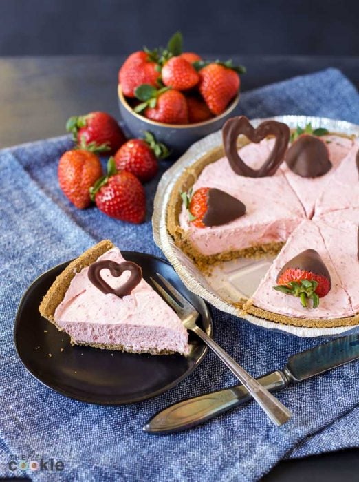 slice of vegan strawberry cheesecake on a black plate topped with chocolate heart