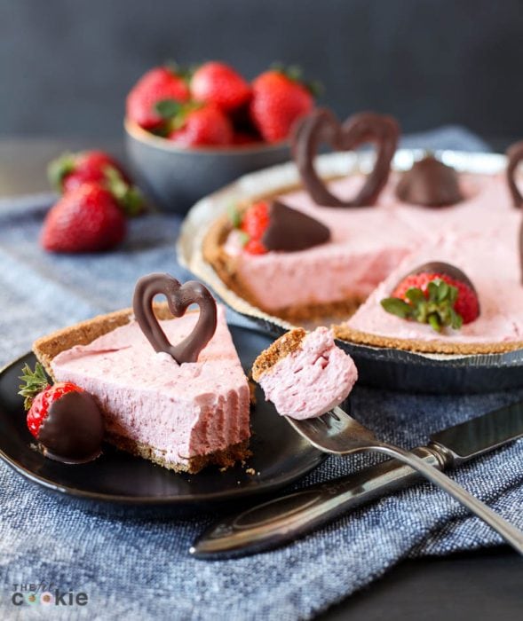 strawberry vegan cheesecake slice on a black plate with a bite taken