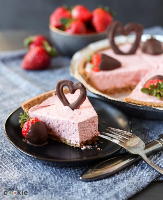 slice of strawberry vegan cheesecake on a black plate topped with a chocolate heart