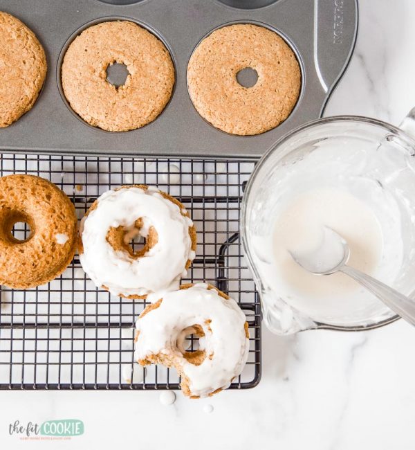 overhead photo of vegan carrot cake donuts in a pan and on a wire rack with cream cheese glaze