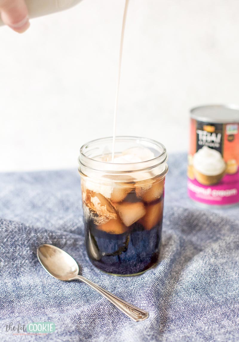 photo of coffee creamer being poured into a glass of cold brew coffee with ice.