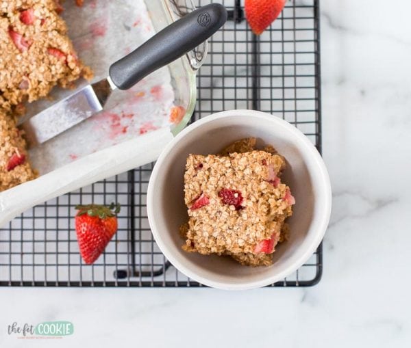 overhead photo of baked oatmeal with strawberries in a white bowl on a black cooling rack
