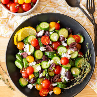 Greek salad with cucumbers, tomatoes and feta cheese served in a black bowl.