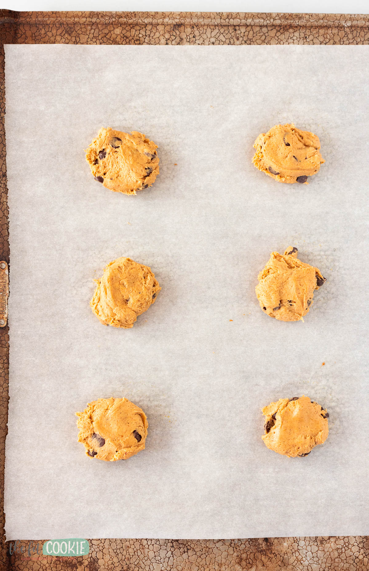 Six scoops of pumpkin chocolate chip cookie dough, spaced evenly on a parchment-lined baking sheet, ready to be baked.