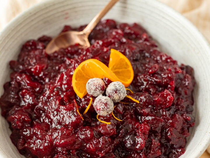 A bowl of Instant Pot cranberry sauce garnished with sugared cranberries and orange slices.