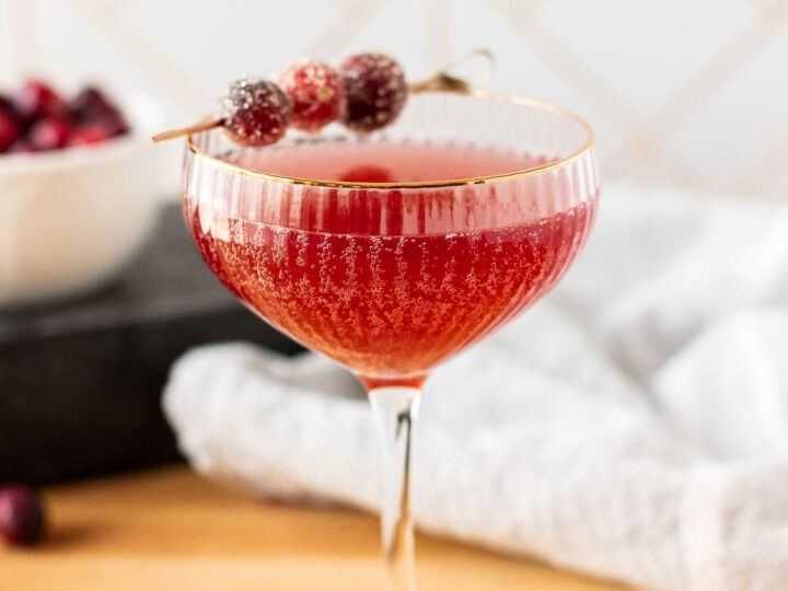 A champagne glass filled with a red cranberry apple mocktail garnished with sugared cranberries.
