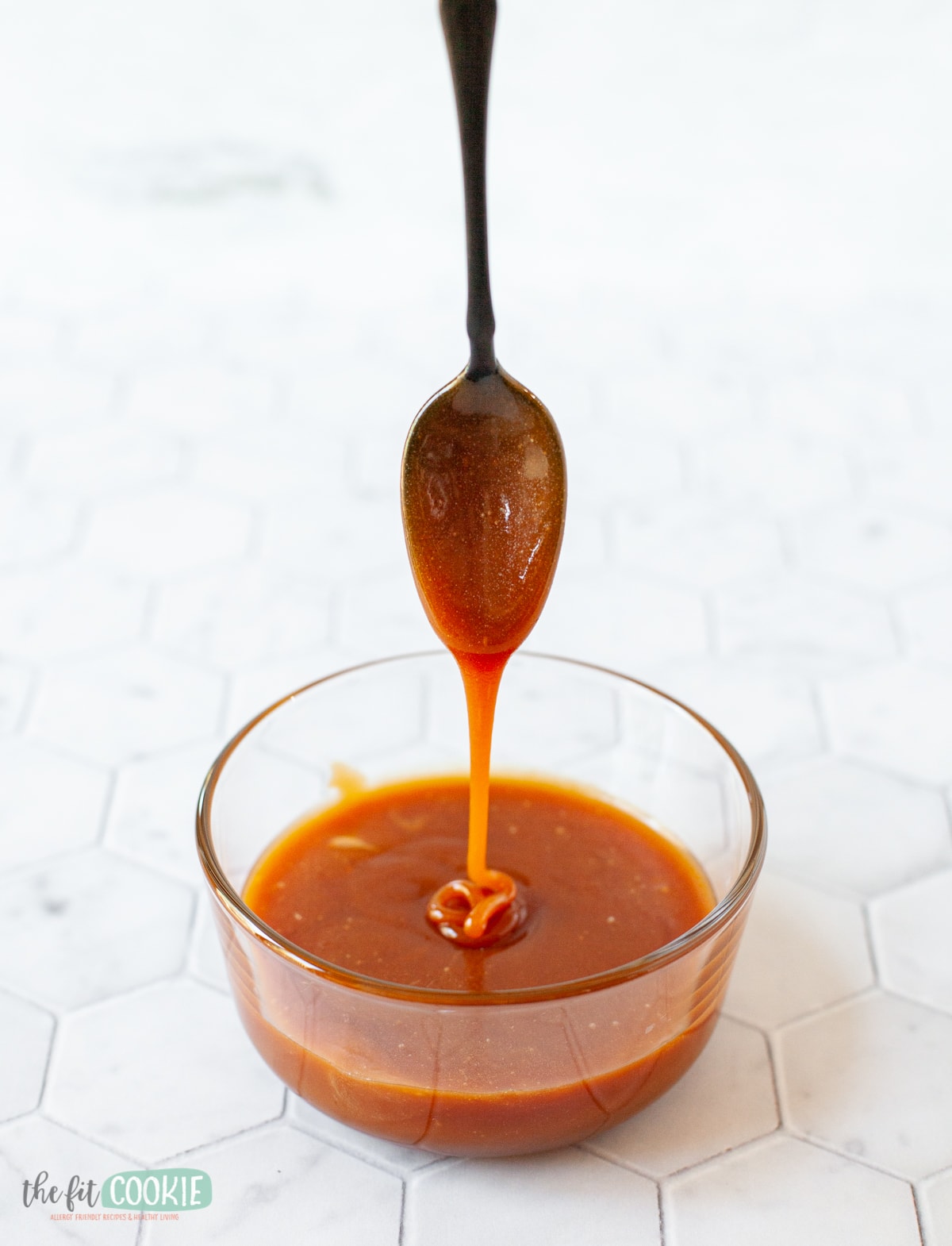 photo of black spoon drizzling dairy free caramel sauce into glass dish.
