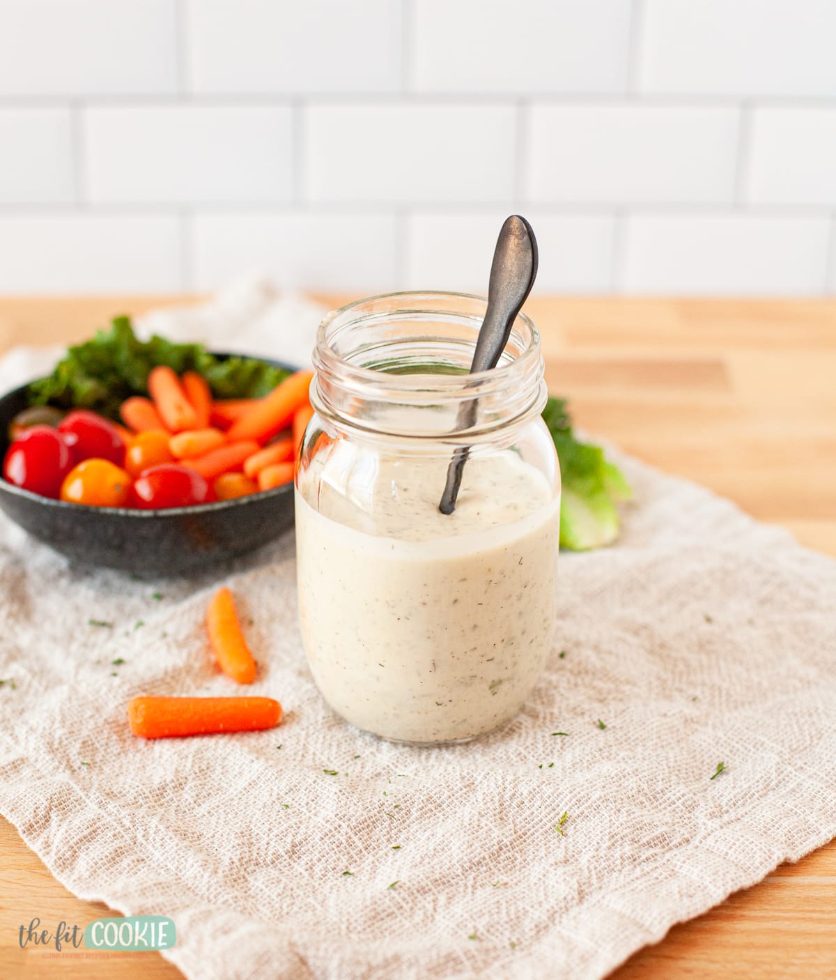 glass jar of dairy free ranch dressing next to a bowl of veggies