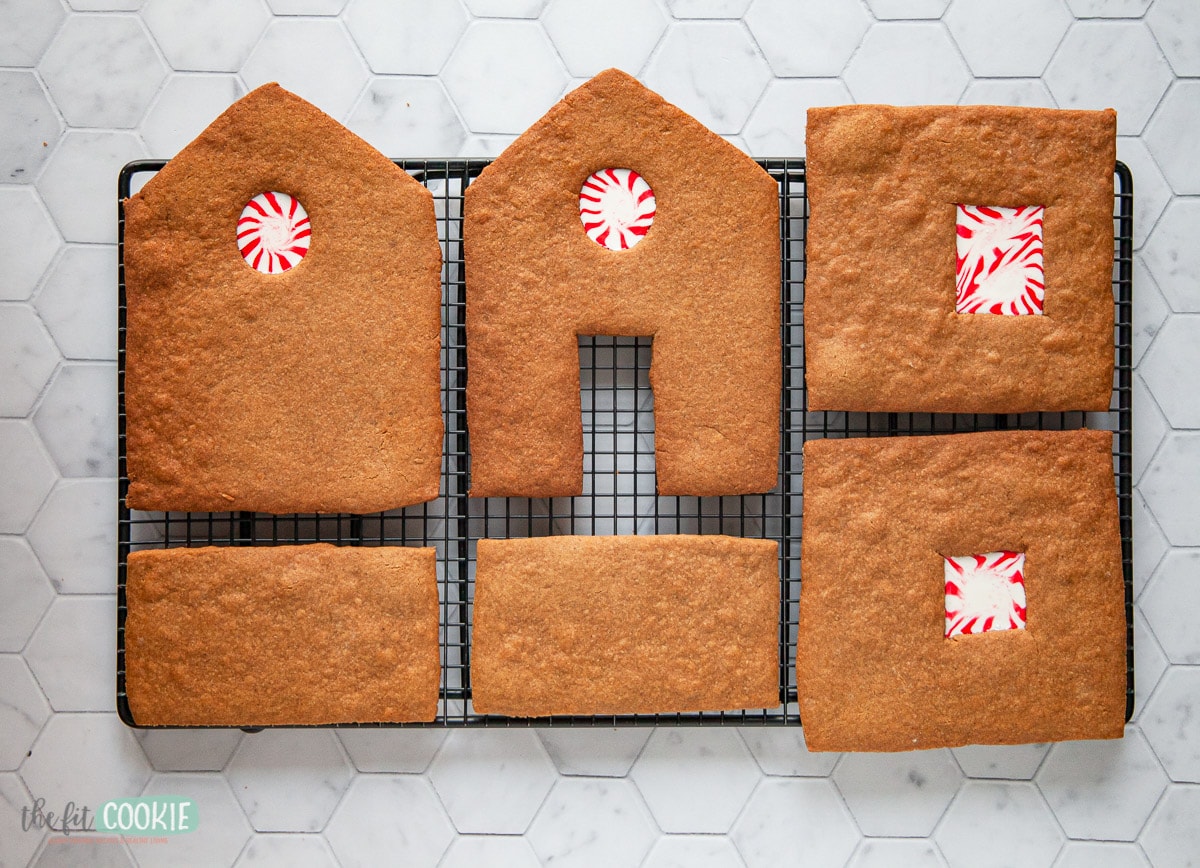 pieces of gingerbread house on a black cooling rack with peppermint candy in the windows