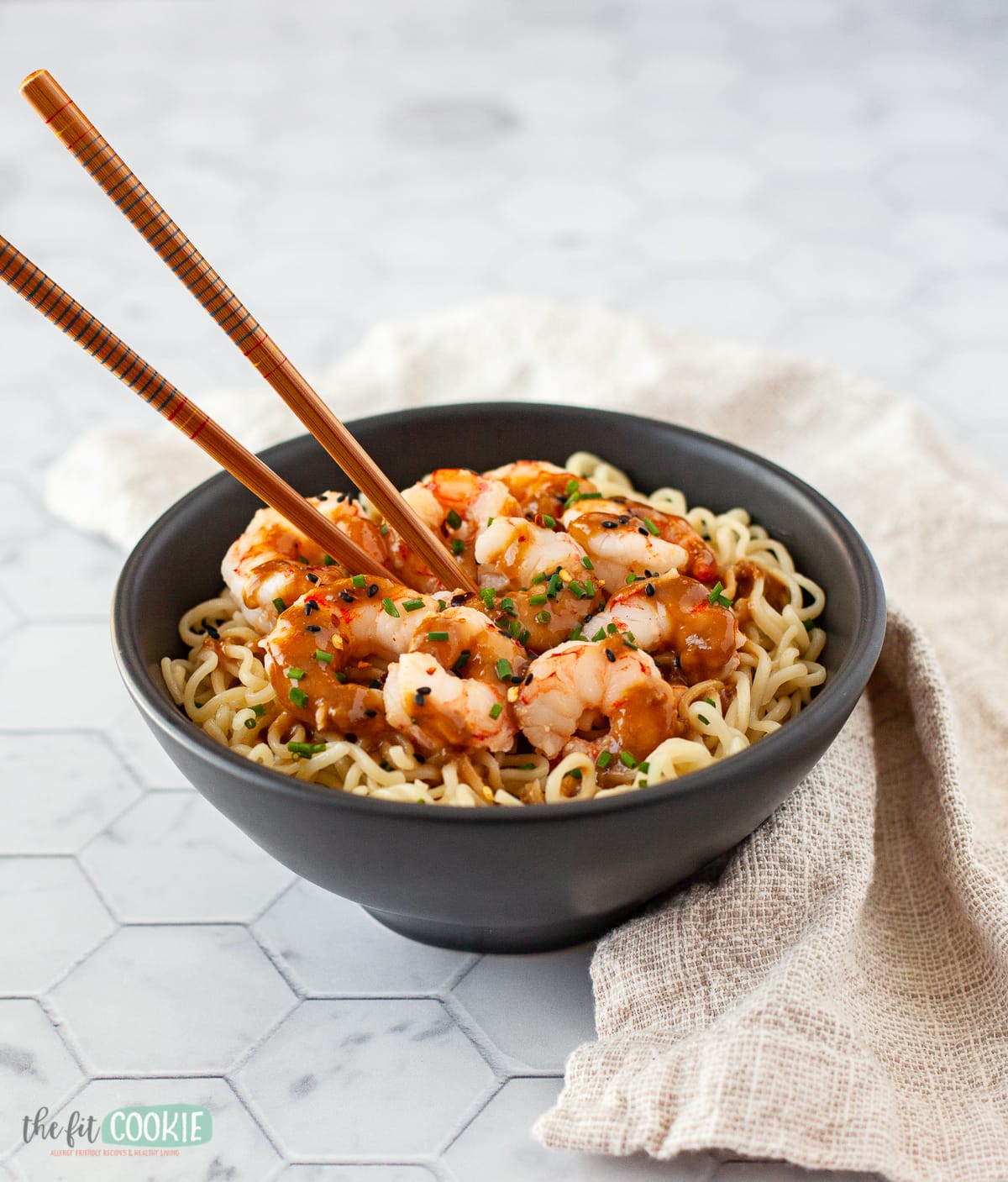 black bowl filled with shrimp and noodles with bamboo chopsticks.