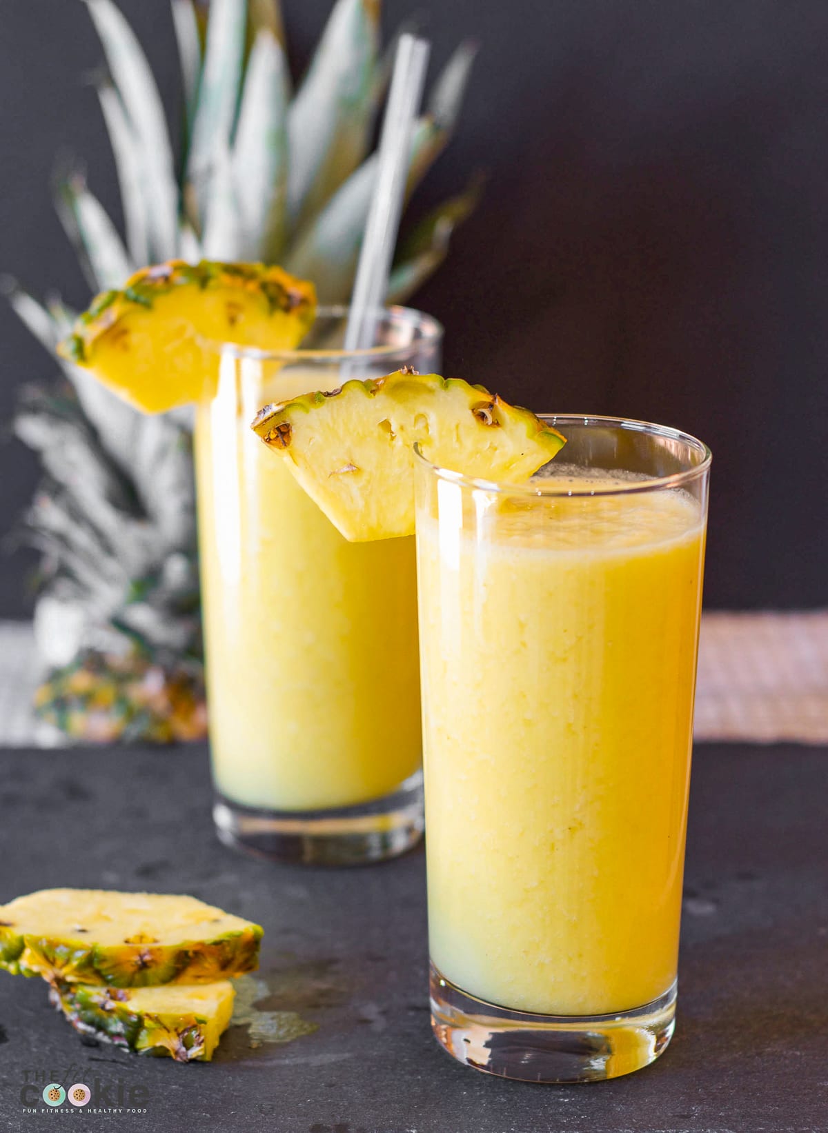 2 tall glasses filled with pineapple smoothie with pieces of pineapple on the rim of the glass. 