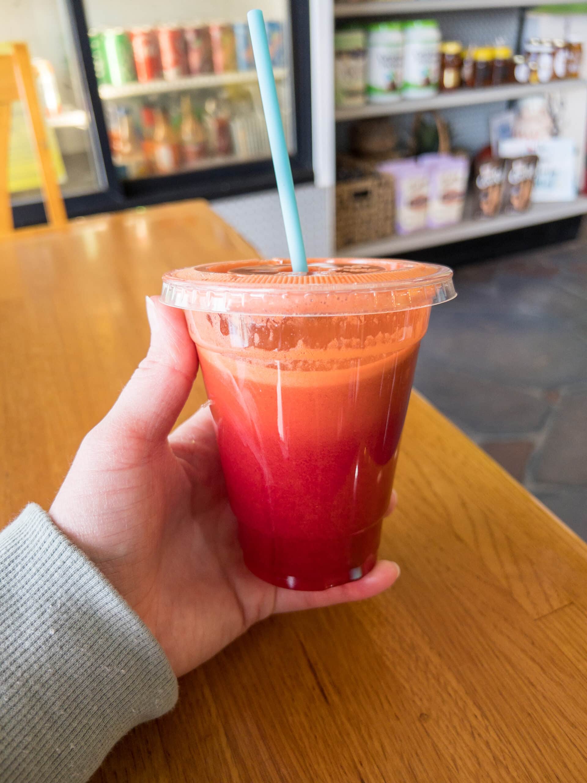 photo of hand holding a clear plastic cup filled with fresh pressed fruit and veggie juice that is red colored. 
