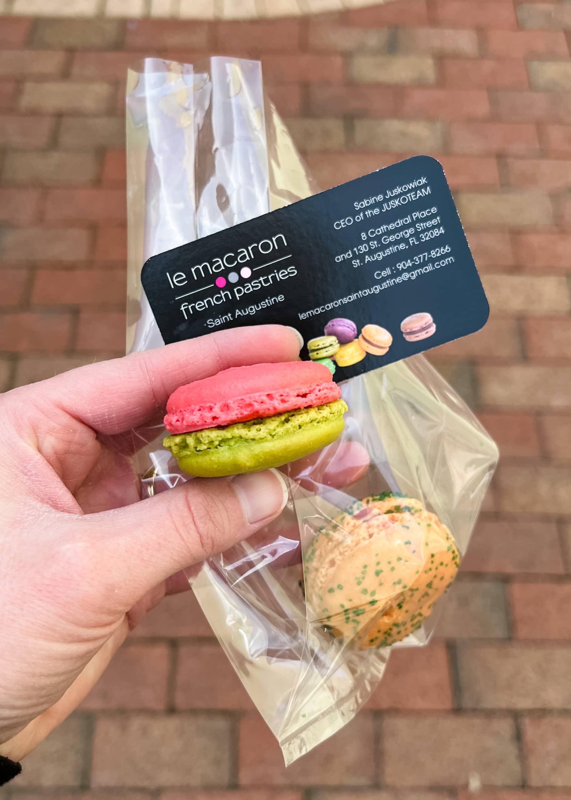 hand holding fruit flavored macarons with a business card for Le Macaron.