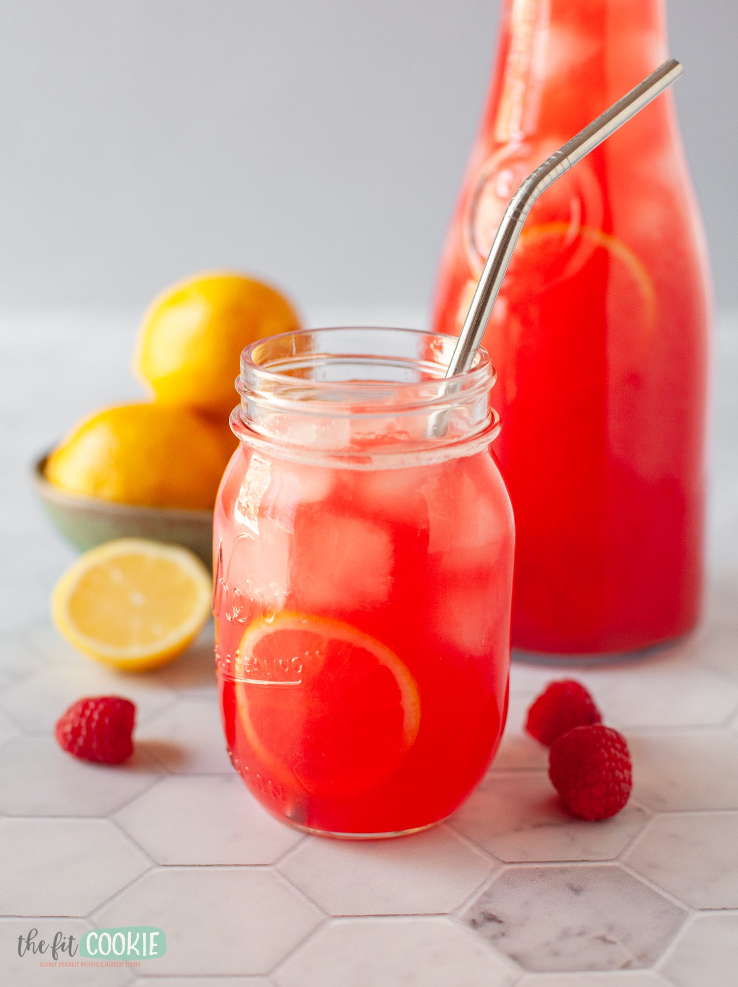 close up photo of raspberry lemonade in a jar with lemons in the background. 