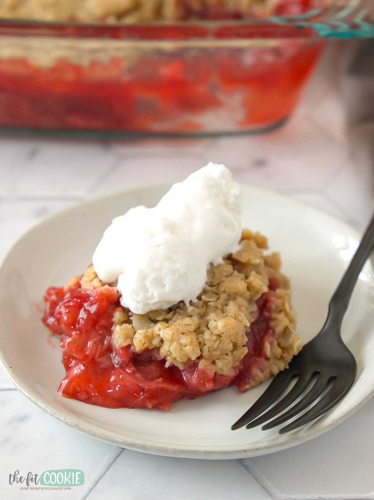 gluten free fruit crisp on a white plate with whipped cream on top.