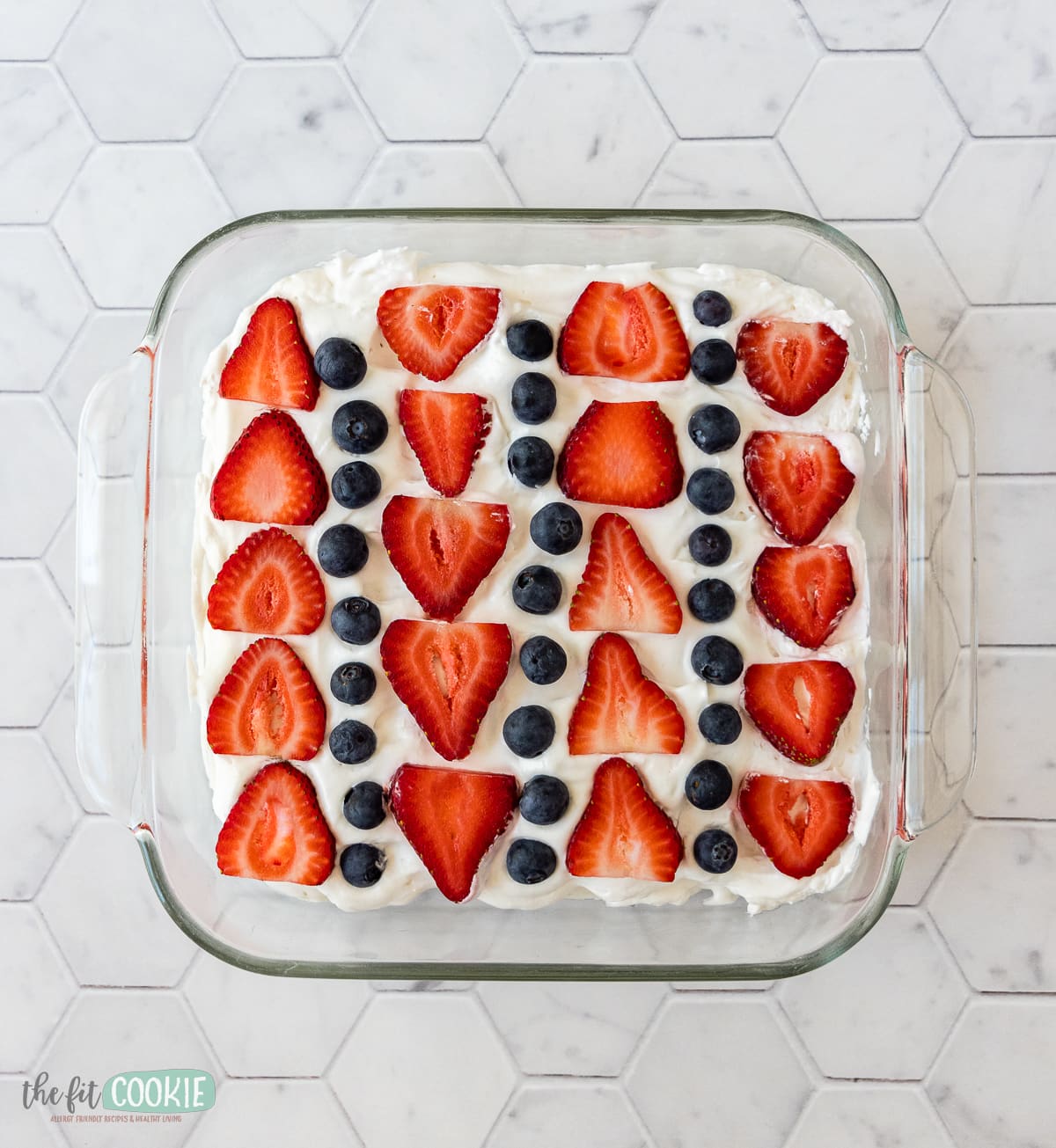 overhead photo of strawberries and blueberries arranged over whipped cream. 