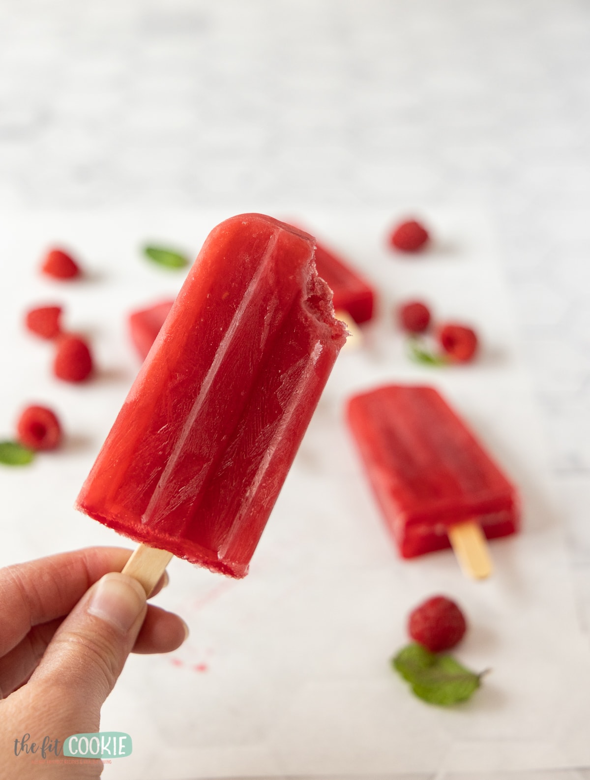 photo of hand holding a red fruit popsicle with a bite taken from the corner. 