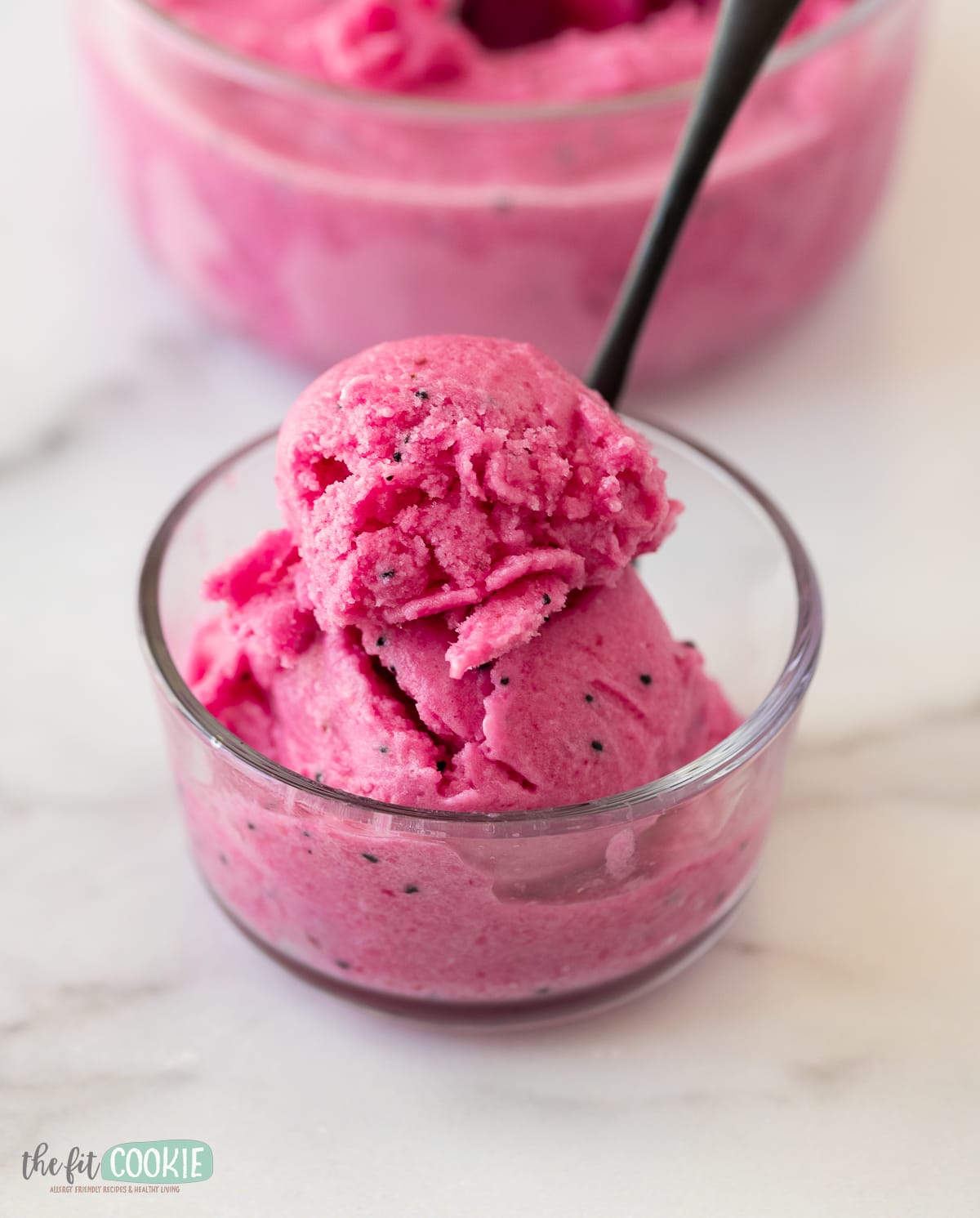 small glass bowl filled with pink pitaya sorbet with a black spoon in it. 