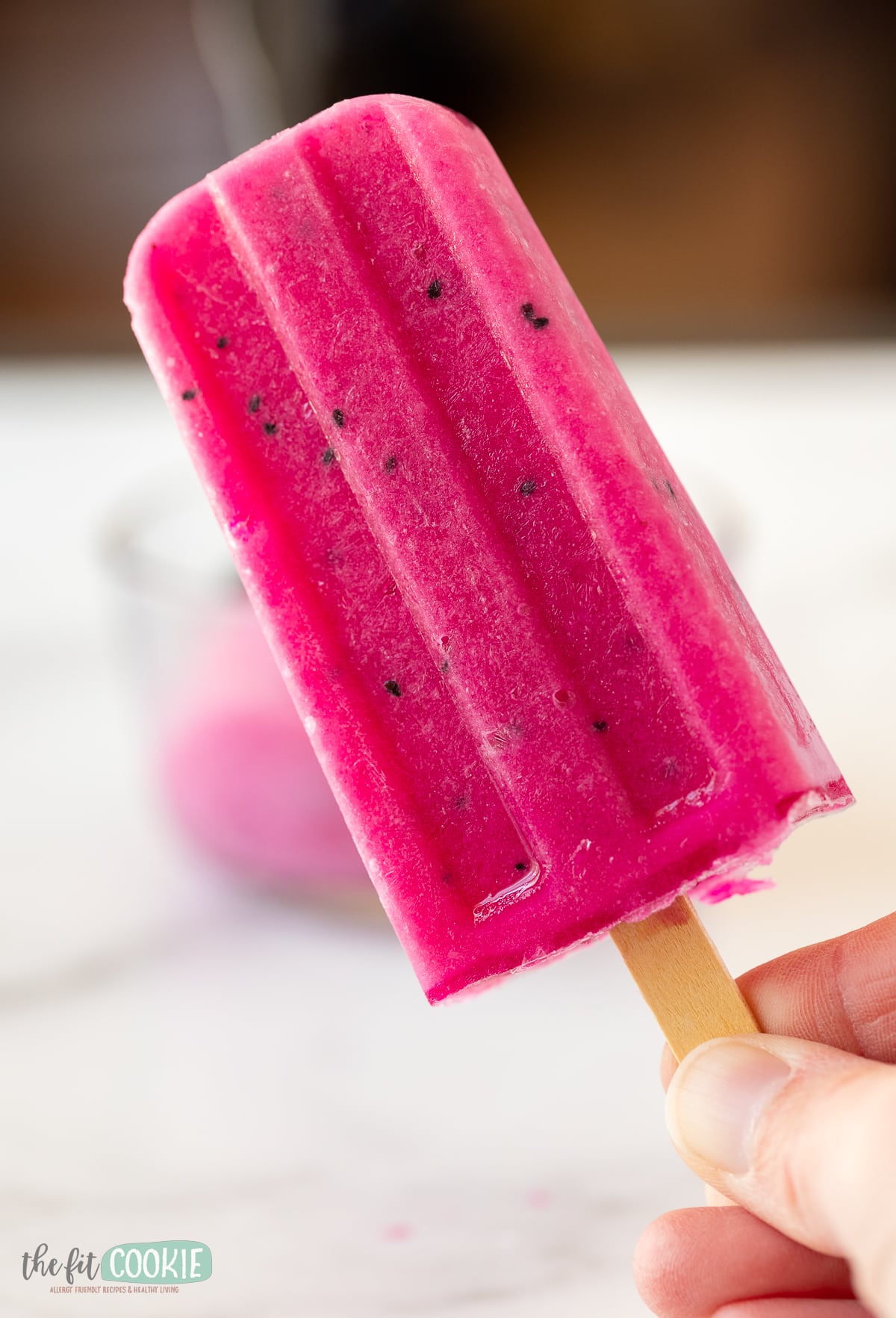 photo of hand holding a pink dragon fruit popsicle. 