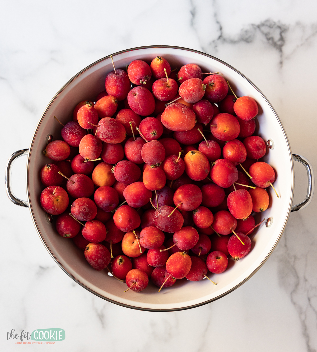 overhead photo of crab apples in a white strainer on a marble surface. 